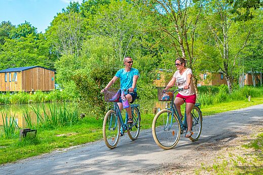 Fietsend stel op groen pad bij vijver op camping CAPFUN La Rivière in Valence-en-Poitou (86).