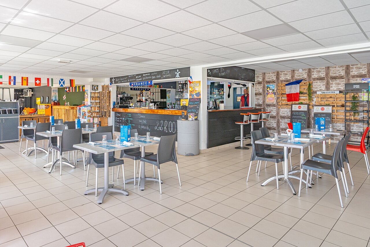 Bar en binnen restaurantruimte met tafels op camping CAPFUN Saint Laurent in LA FORET FOUESNANT (29).