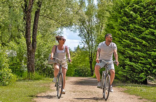 Koppel fietst op groen pad bij camping CLICOCHIC Les Saules de Cheverny.
