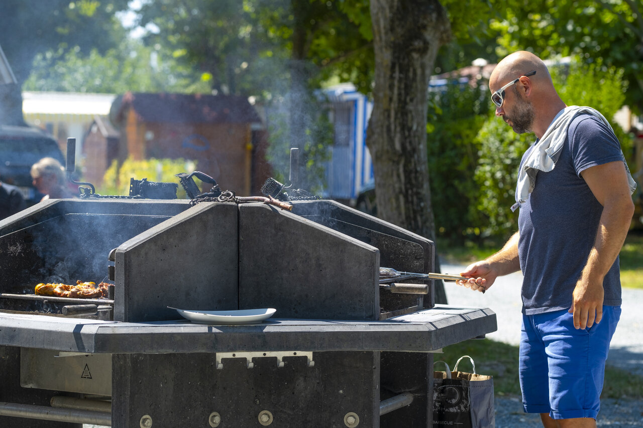 Barbecue op gemeenschappelijke grill, man kookt op camping CLICOCHIC Seuli�res in Saint-Denis-d'Ol�ron.