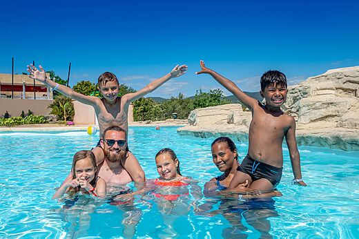 Lachende familie geniet van het buitenzwembad op camping VAGUES OCEANES Soleil de Provence.