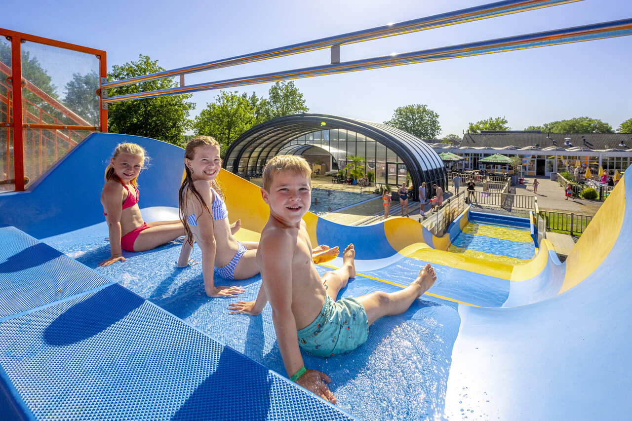 Lachende kinderen op blauw-gele waterglijbaan bij camping CAPFUN De Sprookjescamping in Rheeze.