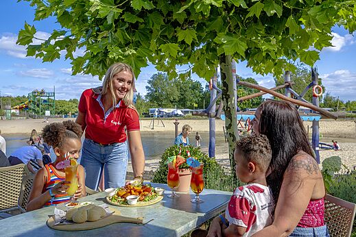 Familie dineert met personeelslid in het restaurant van camping CAPFUN in Rheezerveen