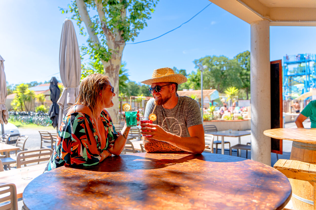 Lachend stel drinkt cocktails aan de bar, zwembad op achtergrond, op camping CLICOCHIC Texas in Argel�s sur Mer (66).