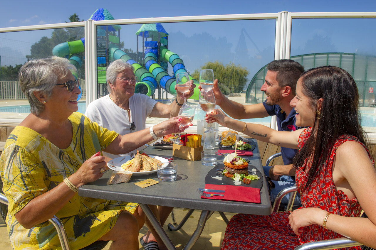 Familie proost op terras, zwembad en glijbanen op camping CAPFUN Celeste in Breuillet (17).