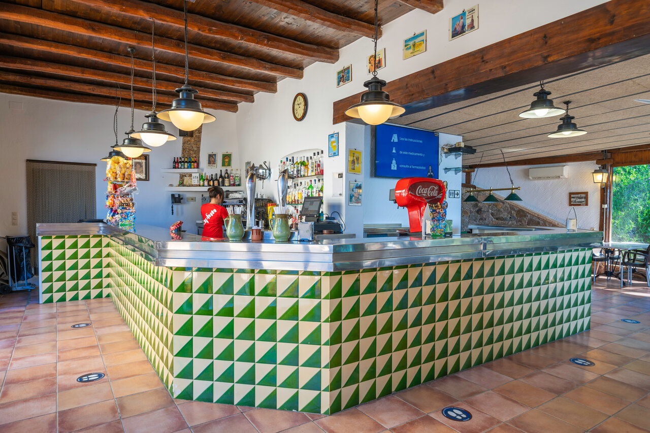 Binnenbar met toonbank en serveerster op camping CAPFUN Treumal in Platja d'Aro.