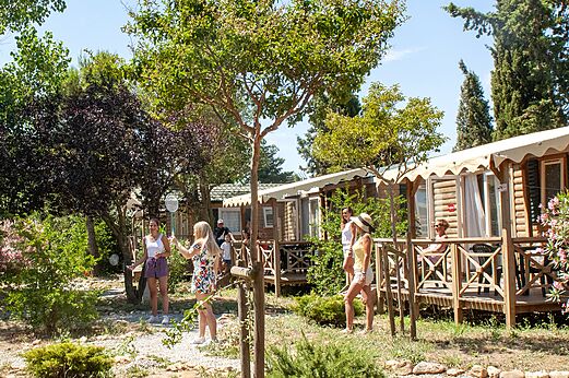 Houten stacaravans met terrassen en mensen die badminton spelen op camping CAPFUN Vignes d'Or in Serignan.