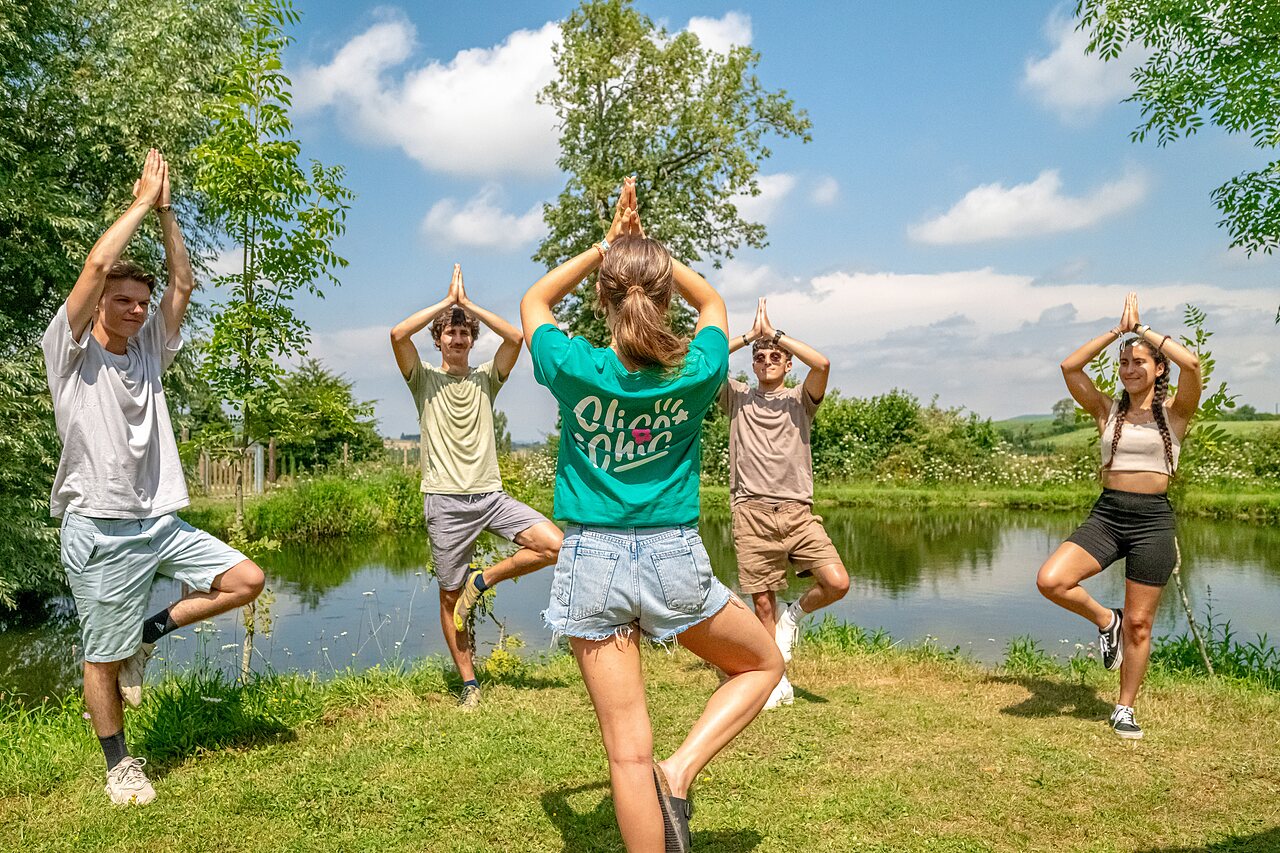 Groep beoefent yoga buiten bij een vijver op camping CLICOCHIC Village des Meuniers in Dompierre-les-Ormes.