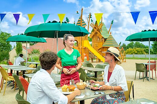 Serveerster en gasten op buitenterras restaurant met speeltuin op camping CLICOCHIC Village des Meuniers in Dompierre-les-Ormes (71).