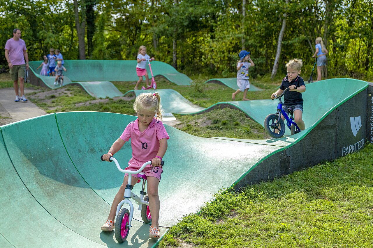 Kinderen spelen op de pumptrack met fietsen en scooters op camping CAPFUN Vlinderloo in Enschede.