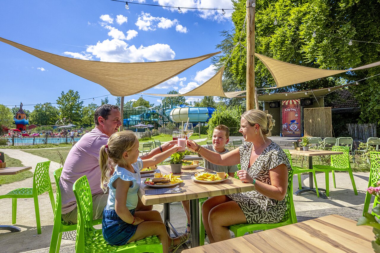 Familie luncht op terras, zwembad en glijbanen op camping CAPFUN Vlinderloo in Enschede.