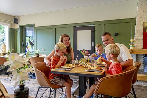 Lachende familie eet maaltijd in het restaurant van camping CAPFUN Vlinderloo in Enschede.