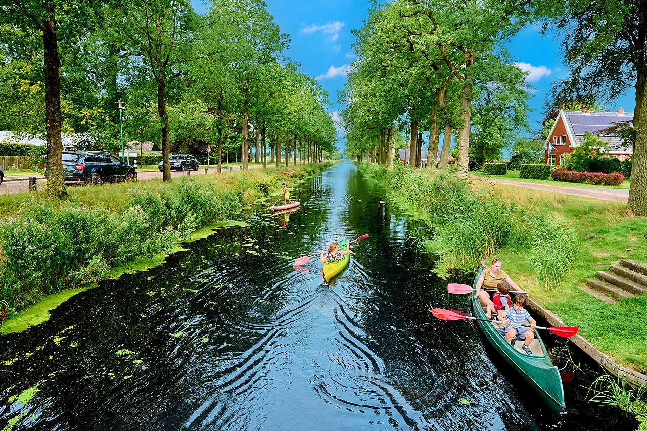 Familie in kano en op paddleboard op het boomrijke kanaal bij camping CAPFUN De Waldsang in Bakkeveen.