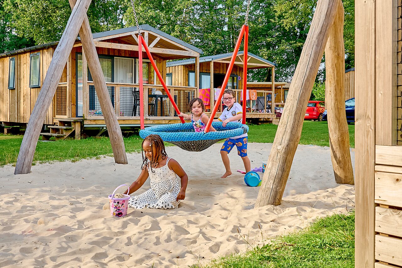 Kinderen spelen op schommel en zand, stacaravans op camping CAPFUN Wieskamp in Winterswijk Henxel.