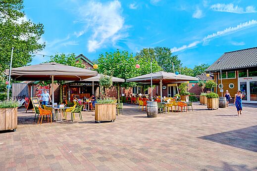 Buitenterras van het restaurant met tafels en parasols op camping CAPFUN Wieskamp.