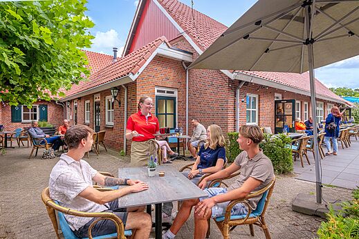 Buitenterras van restaurant met serveerster en gasten op camping CAPFUN het Winkel in Winterswijk.