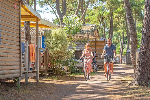 Koppel fietst op pad tussen stacaravans in bos op camping CAPFUN Zephir in Les Mathes La Palmyre (17).