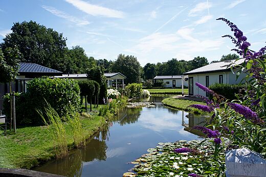 Moderne stacaravans langs een bloemrijke gracht op camping CAPFUN Zeumersehof in Voorthuizen.